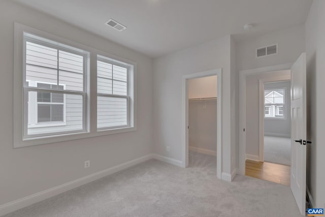 unfurnished bedroom with light colored carpet, a walk in closet, baseboards, and visible vents