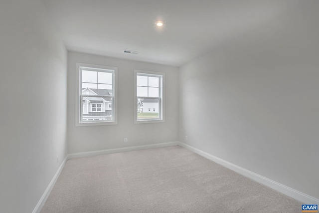 spare room with light colored carpet, visible vents, and baseboards
