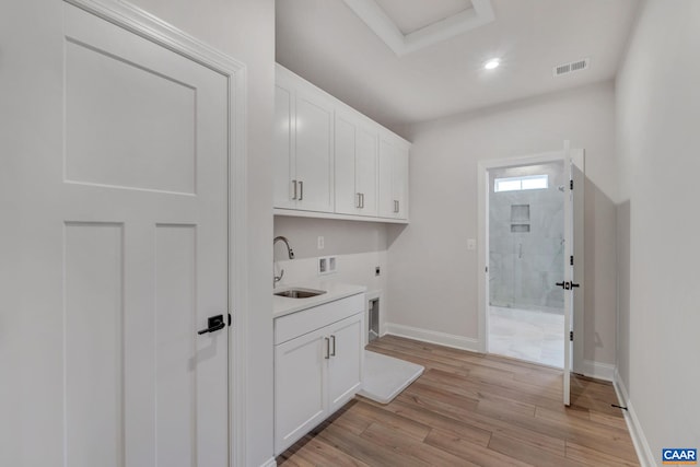clothes washing area featuring light wood finished floors, visible vents, a sink, cabinet space, and electric dryer hookup