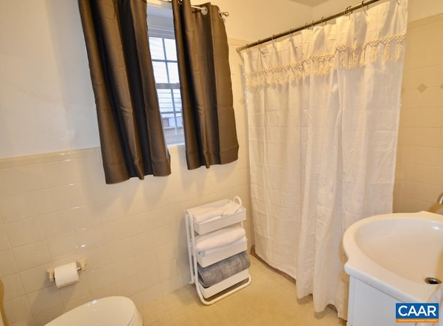 bathroom with tile walls, toilet, a sink, curtained shower, and a wainscoted wall