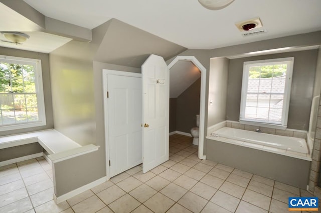 full bathroom with vaulted ceiling, tile patterned flooring, toilet, and a garden tub