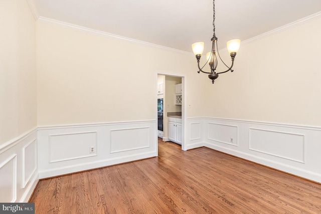  - empty room with a chandelier, crown molding, light wood-style flooring, and wainscoting