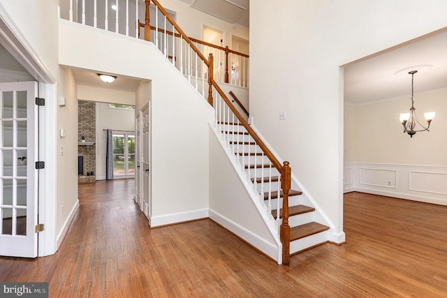  - stairs with a chandelier, wood finished floors, a fireplace, and a towering ceiling