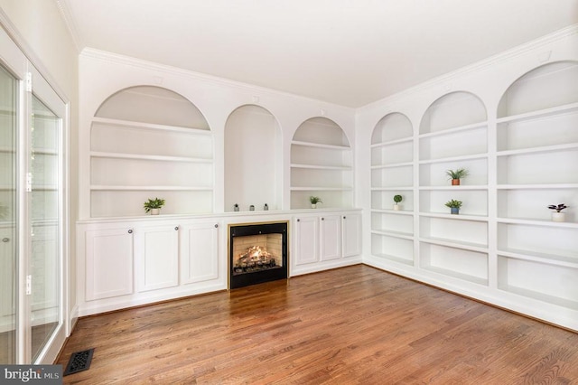  - unfurnished living room with a lit fireplace, light wood-style flooring, built in shelves, and crown molding