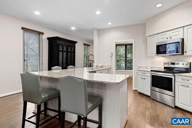 kitchen with a sink, stainless steel appliances, a kitchen bar, dark wood-style floors, and white cabinets
