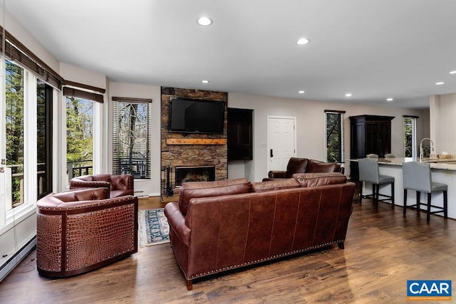 living room with dark wood-style floors, a baseboard radiator, a stone fireplace, and recessed lighting
