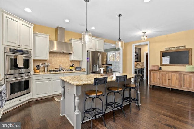 11135 Vanderbilt Cv, Spotsylvania, VA 22551 - kitchen featuring appliances with stainless steel finishes, wall chimney exhaust hood, dark wood finished floors, white cabinetry, and a center island