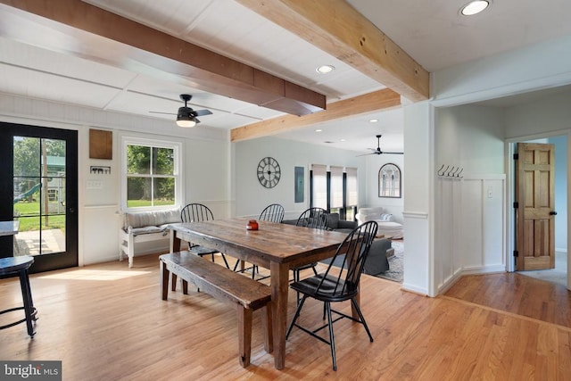  - dining area with a ceiling fan, light wood-style flooring, beamed ceiling, plenty of natural light, and a wainscoted wall