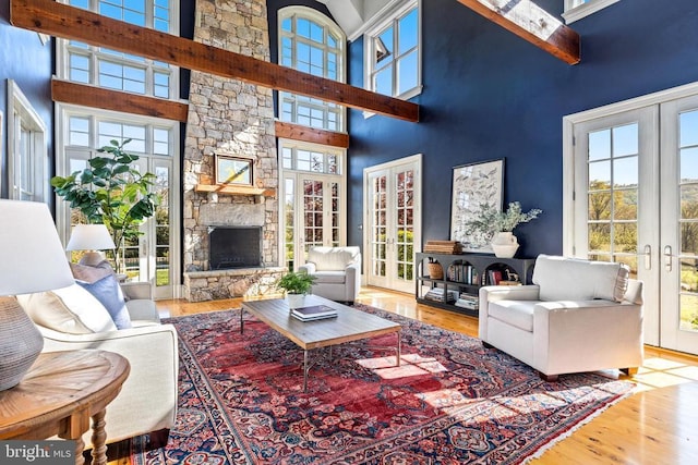  - living room with a towering ceiling, wood finished floors, a stone fireplace, healthy amount of natural light, and french doors