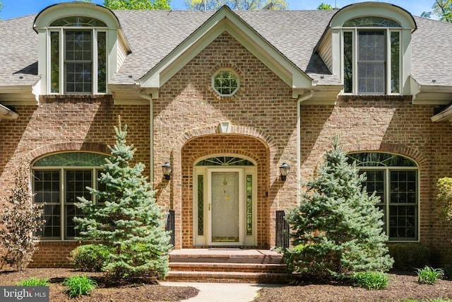  - doorway to property featuring brick siding and roof with shingles