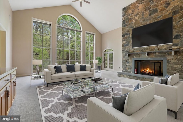  - carpeted living room with a stone fireplace, a ceiling fan, a healthy amount of sunlight, and high vaulted ceiling