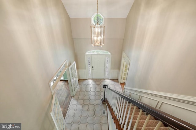  - foyer entrance with a wainscoted wall, a decorative wall, high vaulted ceiling, and a notable chandelier