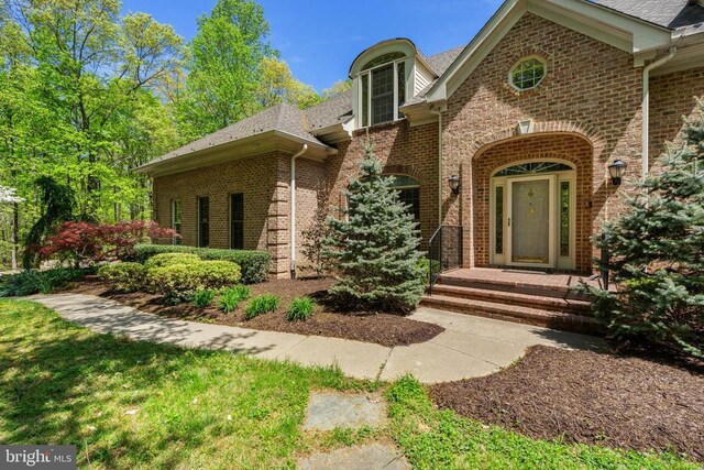  - entrance to property with roof with shingles and brick siding