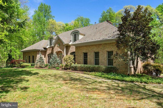  - french provincial home featuring roof with shingles, a chimney, brick siding, and a front yard