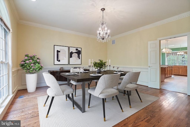  - dining room featuring an inviting chandelier, a wainscoted wall, crown molding, visible vents, and light wood-style floors