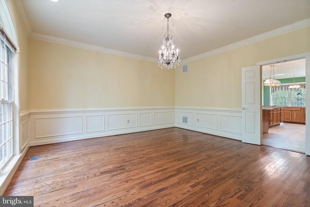  - unfurnished room with a wainscoted wall, wood finished floors, visible vents, crown molding, and a notable chandelier