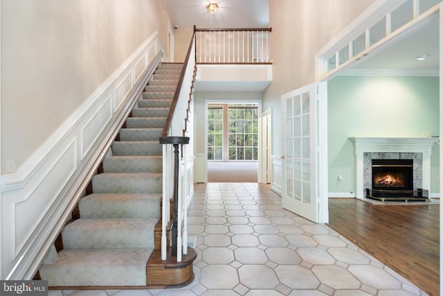  - stairs featuring french doors, a decorative wall, a towering ceiling, and a fireplace