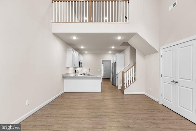 5711 Finley Rose Ct, Fredericksburg, VA 22407 - kitchen with white cabinets, light wood-style flooring, a peninsula, appliances with stainless steel finishes, and light stone counters