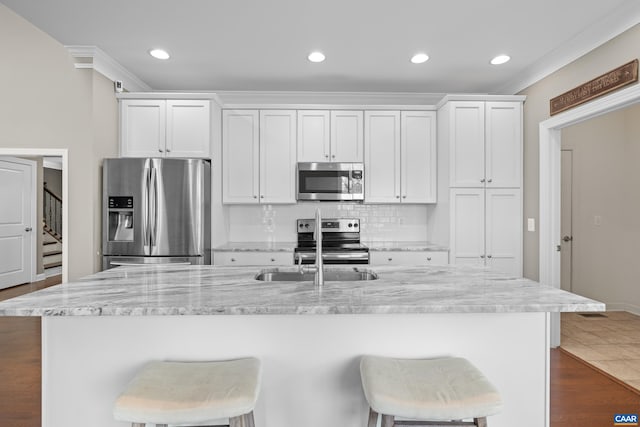kitchen featuring appliances with stainless steel finishes, white cabinetry, a kitchen breakfast bar, decorative backsplash, and an island with sink