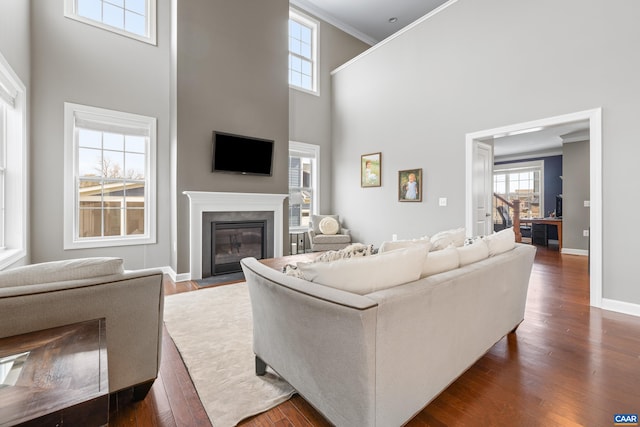 living room featuring a fireplace with flush hearth, crown molding, dark wood-type flooring, baseboards, and a towering ceiling