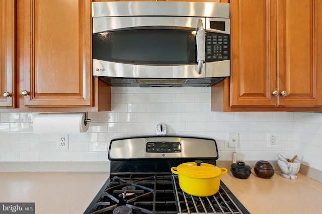 kitchen with stainless steel appliances, light countertops, backsplash, and brown cabinetry
