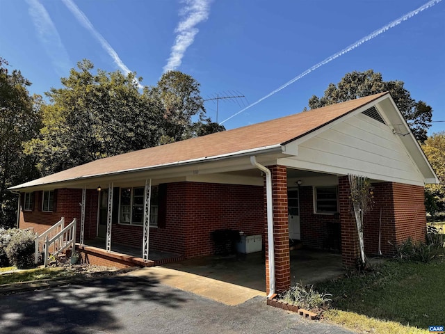 view of side of home with driveway, an attached carport, a porch, and brick siding