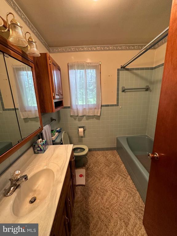 bathroom featuring tile walls, vanity, toilet, a wainscoted wall, and bathing tub / shower combination