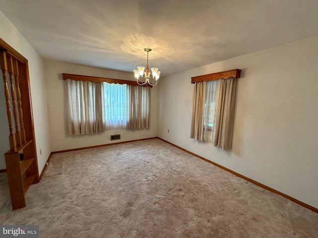 carpeted empty room featuring a chandelier and baseboards
