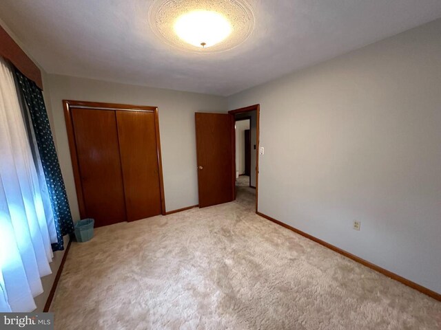 unfurnished bedroom with light carpet, a closet, and baseboards