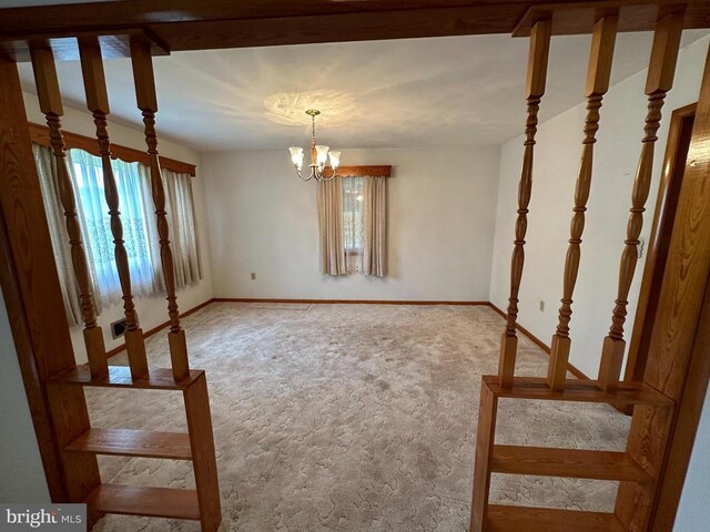 carpeted spare room featuring a chandelier and baseboards
