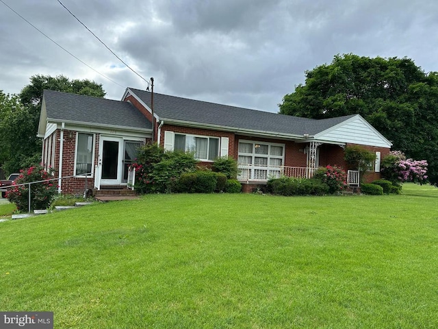 single story home featuring brick siding, a front lawn, roof with shingles, and covered porch