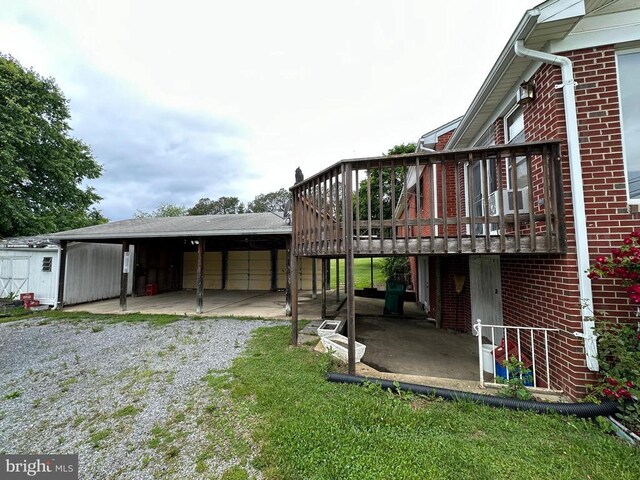 back of house featuring brick siding, an outdoor structure, driveway, and a wooden deck
