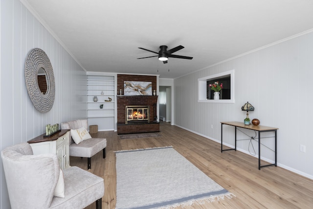 living room featuring crown molding, a ceiling fan, wood finished floors, a brick fireplace, and baseboards