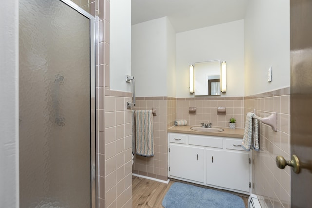 bathroom featuring tile walls, a stall shower, wood finished floors, vanity, and a wainscoted wall
