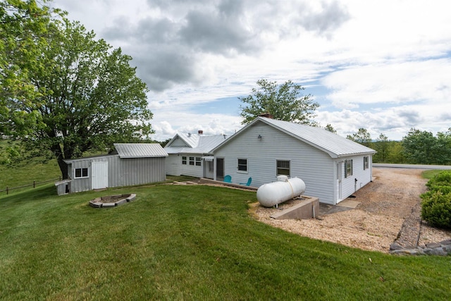 back of property featuring metal roof, an outdoor structure, a fire pit, and a chimney