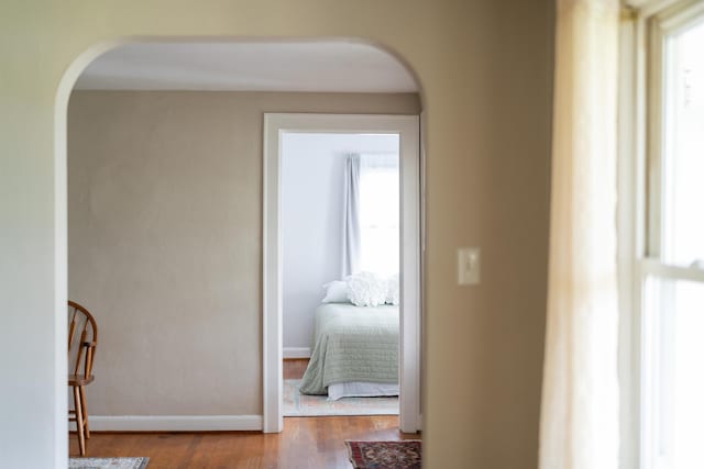 hallway with arched walkways, wood finished floors, and baseboards