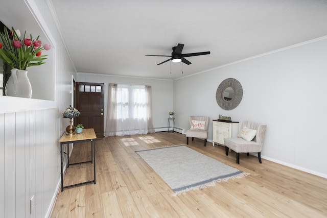sitting room with ornamental molding, baseboard heating, light wood-style floors, ceiling fan, and baseboards