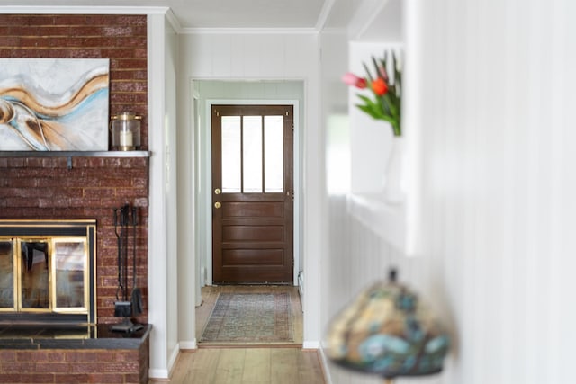 entryway with ornamental molding, wood finished floors, baseboards, and a brick fireplace