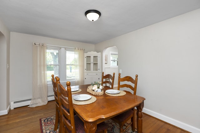 dining area featuring arched walkways, baseboards, wood finished floors, and baseboard heating