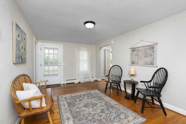 living area with arched walkways, a baseboard heating unit, wood finished floors, and baseboards