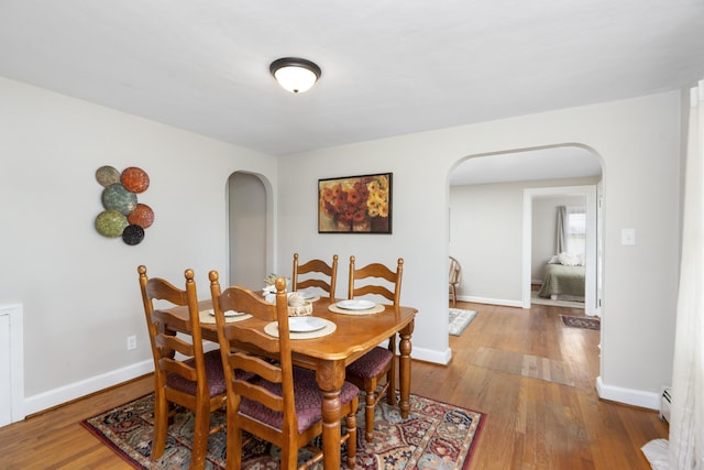 dining space featuring arched walkways, wood finished floors, and baseboards
