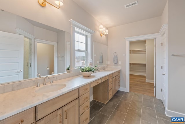 bathroom with baseboards, visible vents, a sink, double vanity, and a spacious closet