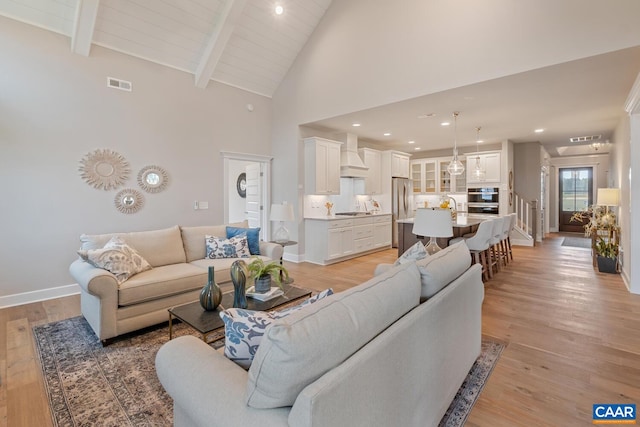 living area featuring baseboards, light wood finished floors, beam ceiling, and visible vents