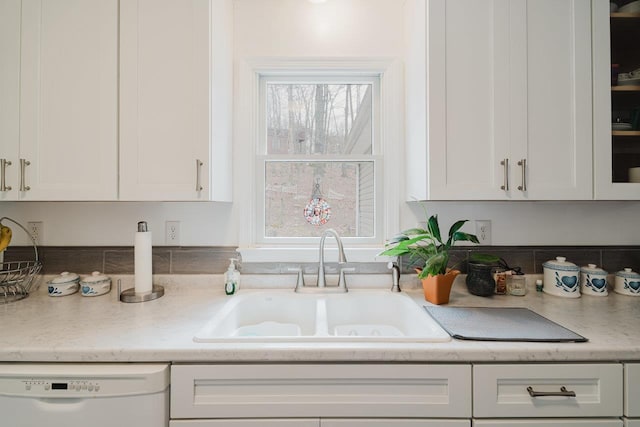 kitchen with white cabinetry, white dishwasher, light countertops, and a sink