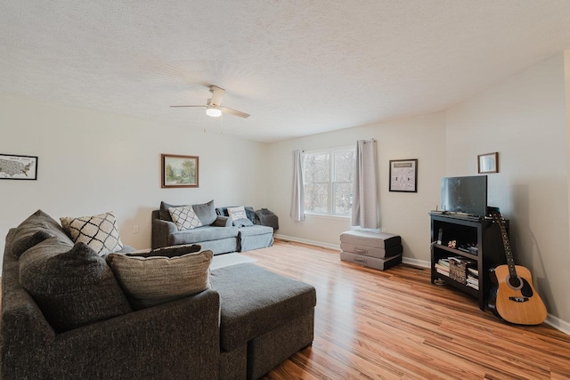 living room with a textured ceiling, baseboards, a ceiling fan, and light wood-style floors