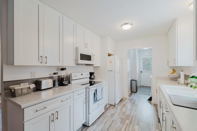 kitchen with white cabinets, light wood-style flooring, a sink, and white appliances