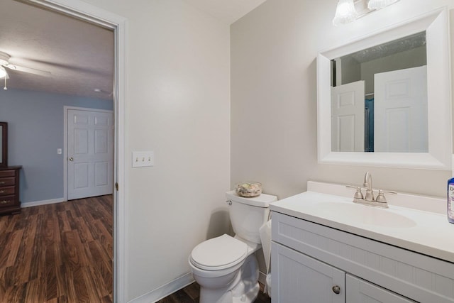 bathroom with toilet, wood finished floors, baseboards, ceiling fan, and vanity