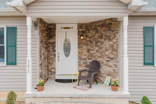 view of exterior entry with a porch, a shingled roof, and stone siding
