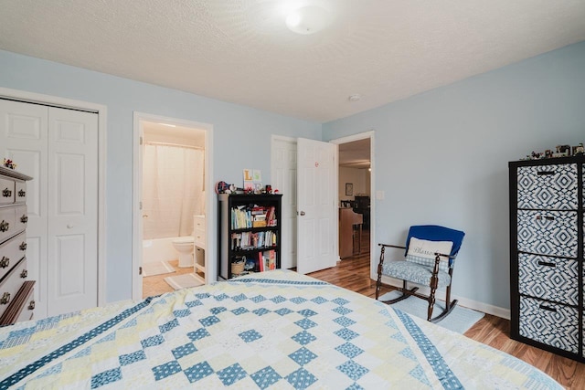 bedroom with baseboards, ensuite bathroom, a closet, and wood finished floors