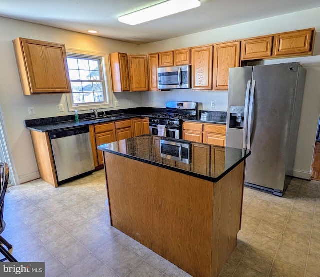 kitchen with stainless steel appliances, a sink, a center island, dark stone counters, and brown cabinetry
